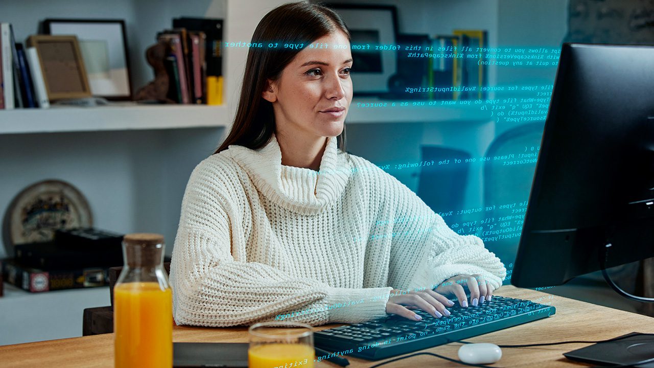 A young woman with long brown hair and light skin is sitting at a desk, typing on a keyboard while looking at a computer screen. She is wearing a cozy white turtleneck sweater and has a focused expression. Floating blue digital code overlays the image, giving a futuristic or tech-themed effect. The workspace includes a wooden desk with a glass of orange juice and a bottle of juice nearby. In the background, there is a white bookshelf filled with books, picture frames, and decorative items. The setting suggests a home office or remote work environment.