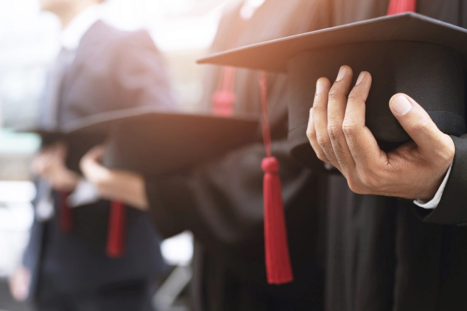 Graduates wearing academic gowns holding their mortarboards with red tassels during a commencement ceremony.
