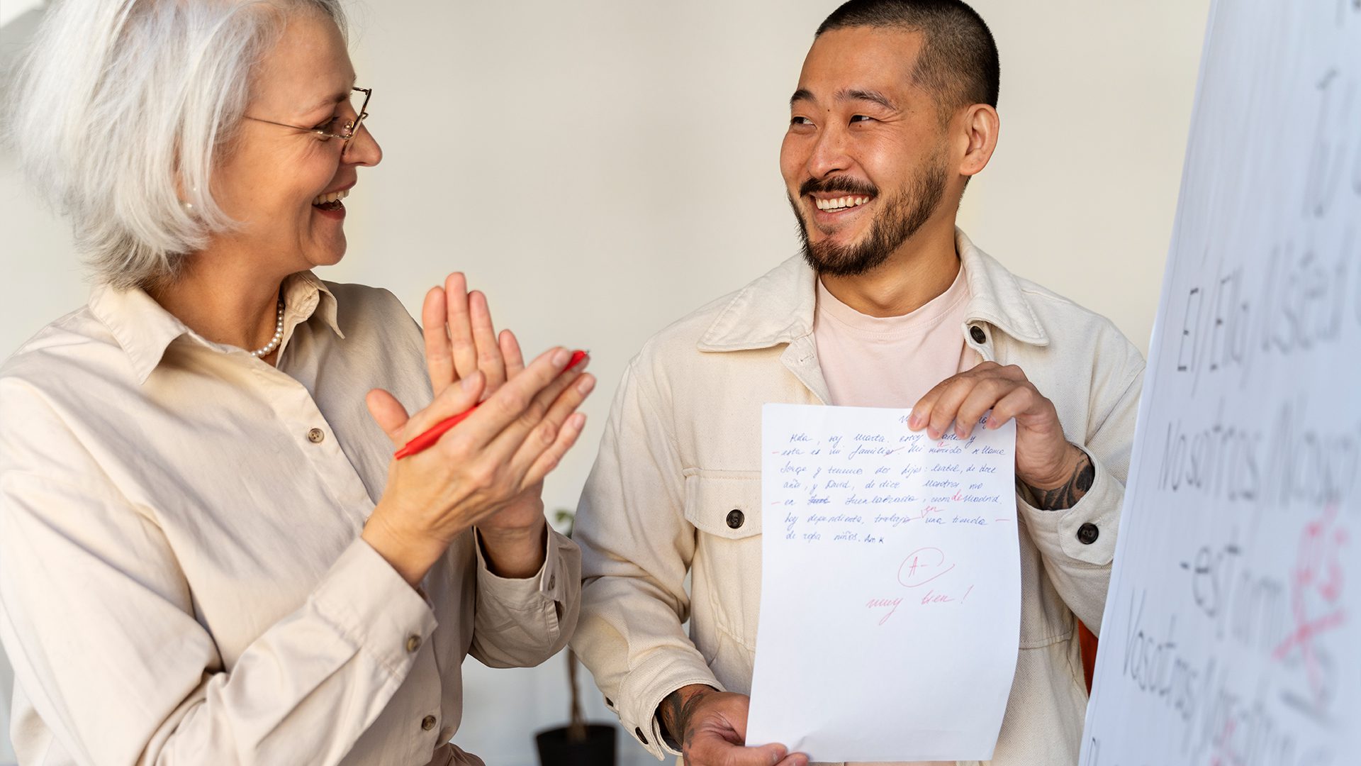 A man and woman smile and clap while proudly holding up a piece of paper.